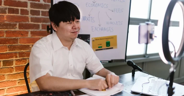 Man engaged in cryptocurrency blogging, using a ring light, microphone, and laptop, with a focus on