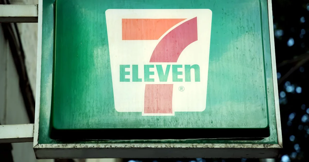 A close-up of a 7-Eleven store sign in a city environment, outdoors.