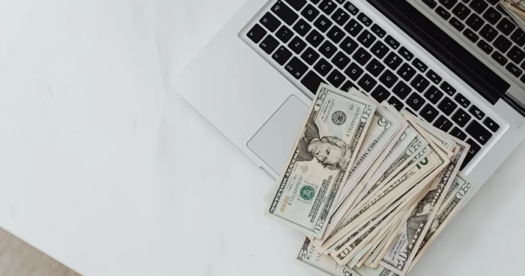Close-up of US dollar bills scattered on a laptop keyboard on a white desk, symbolizing digital fina