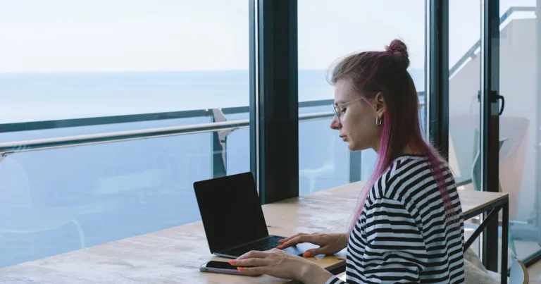 A woman with a laptop working remotely by the ocean, embracing the digital nomad lifestyle.