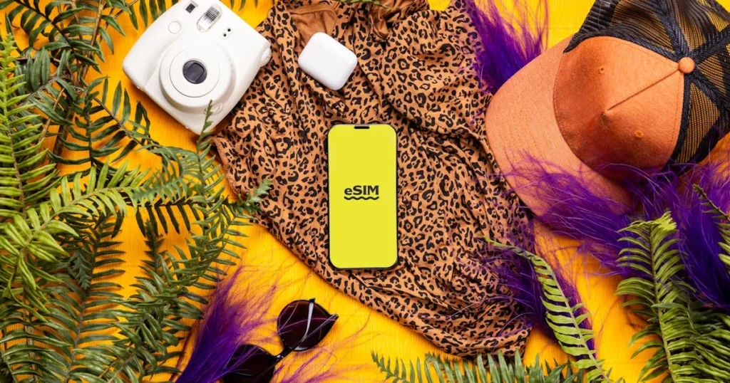 Flat lay of summer travel essentials featuring a leopard print dress, gadgets, and greenery on a bri