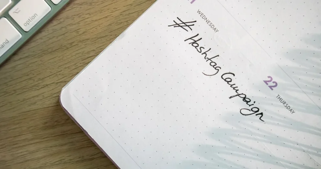 Open planner with 'Hashtag Campaign' handwritten next to keyboard. Ideal for social media and produc