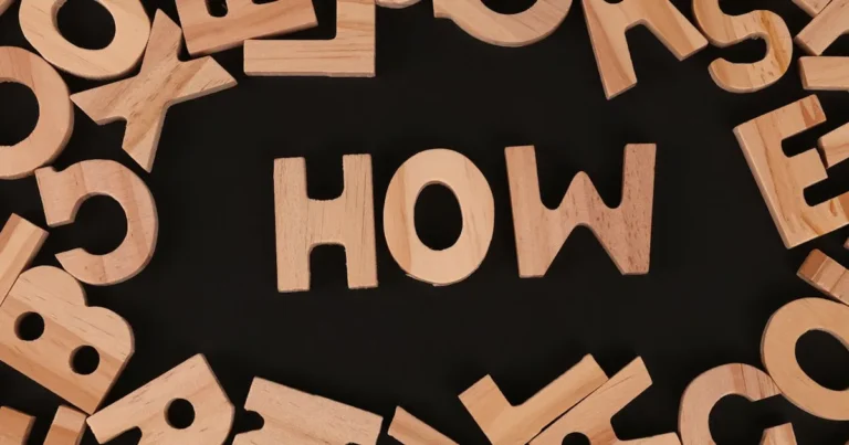Top view of scattered wooden letters with 'HOW' centered on a dark surface, promoting inquiry.