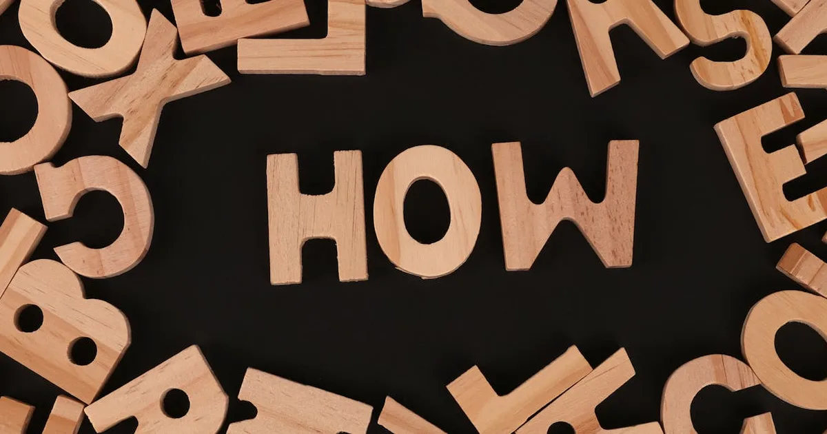 Top view of scattered wooden letters with 'HOW' centered on a dark surface, promoting inquiry.