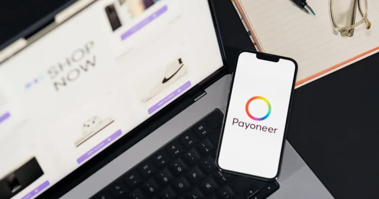 Mobile phone with Payoneer app on screen next to laptop displaying online shopping site.
