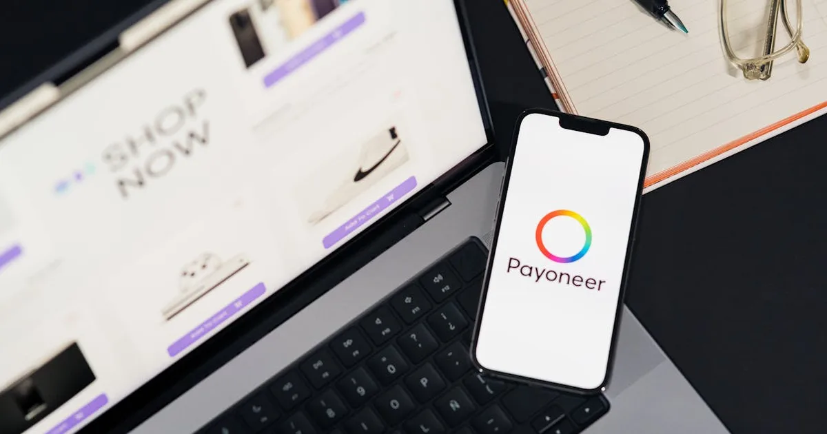 Mobile phone with Payoneer app on screen next to laptop displaying online shopping site.